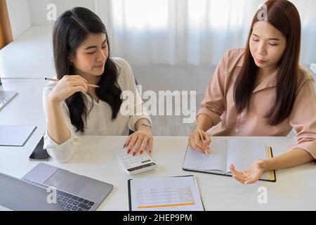 Two business colleagues women working together in the office. Female accountant brainstorming in their workstation. Stock Photo