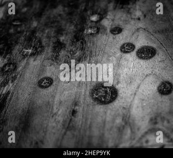 A close-up shot of textured tabletop made of wood with a black burnt spot in black and white. Stock Photo
