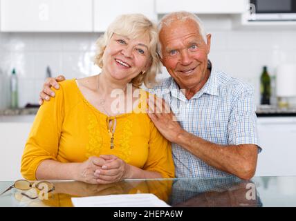 Positive elderly family couple sitting at kitchen table Stock Photo