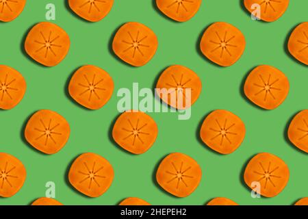 Pattern of slices ripe orange persimmon on a green background. Seamless pattern Stock Photo