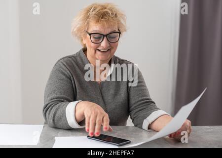 An elderly woman fills a receipt for payment of utility bills. Stock Photo