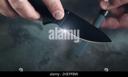 Man sharpening his pocket knife with a whetstone on a rustic wooden table  Stock Photo - Alamy