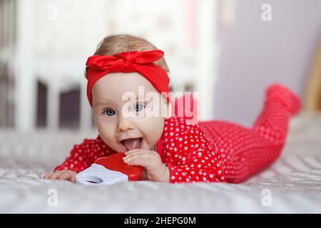 Happy kid lies on bed on stomach. Toddler girl smiling Stock Photo