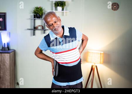 Happy indian senior man got relief after using or wearing back pain relief belt or brace at home - concept of relax from using back supoort belt Stock Photo