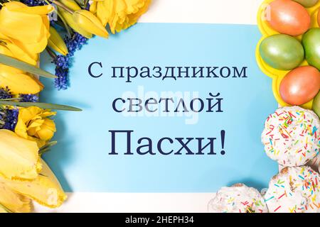 Beautiful postcard with cakes, eggs and flowers with text in Russian, translation from Russian - Happy Easter holiday, top view Stock Photo