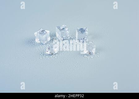 Ice cubes scattered on a table on a gray background in drops of melt water Stock Photo