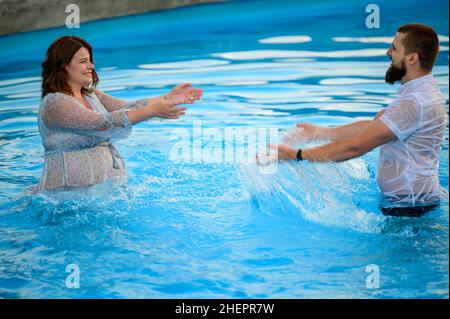 Stryi, Ukraine August 12, 2021: a pregnant woman and her husband swim in the pool, pregnant woman in a dress in the pool. Stock Photo