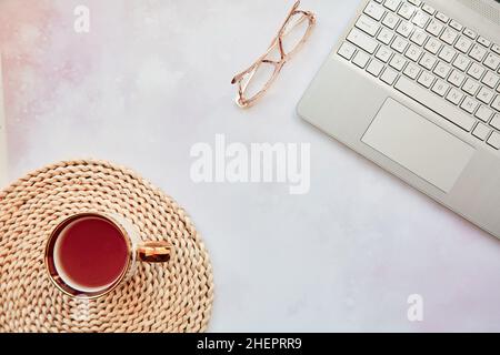 Aesthetic home office: laptop, tea cup and glasses. Feminine concept, remote work, freelance, taking webinar, video calling family because of quarantine concept. Copy space, view from above. Stock Photo