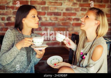 Two happy young female friends with coffee cups enjoying a conversation in a bar Stock Photo