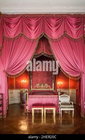 Queen Charlotte Mathilde's bedroom inside Ludwigsburg Residential Palace in Germany. Heavy, red silk damask dominates the room. The bed canopy is espe Stock Photo