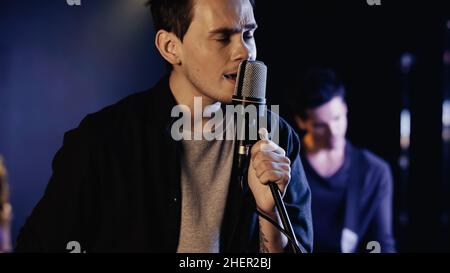 tattooed man singing in microphone near blurred musician on stage,stock image Stock Photo
