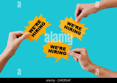 some men hands hold some yellow paper speech bubbles with the text we are hiring written in it, on a blue background Stock Photo