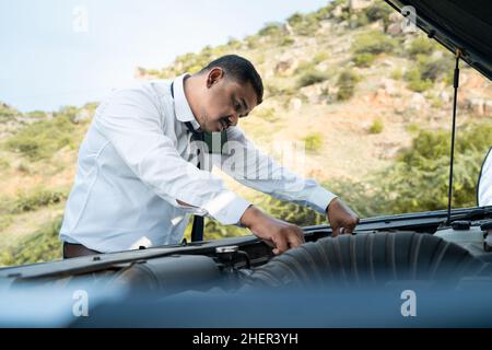 Young bussiness man checking car engine by talking with mechanic on mobile phone at highway road - Concept of businessman asking for a mechanic help Stock Photo