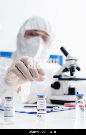 vials with covid-19 omicron vaccine near blurred doctor working near microscope in lab,stock image Stock Photo