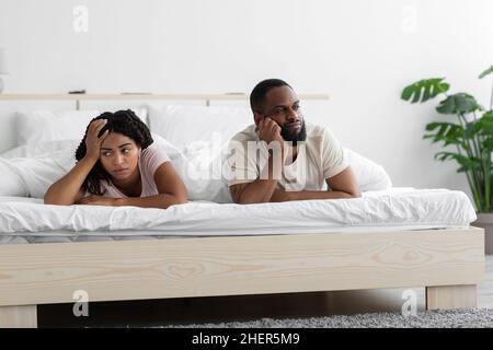 Offended sad unhappy young african american husband ignores wife, lie on comfortable bed in bedroom interior Stock Photo