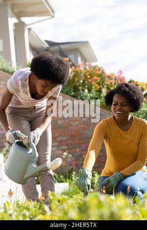 Mother assisting teenage daughter in watering plants at backyard on sunny day Stock Photo