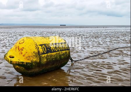Close-up of a weathered, yellow, 'No Mooring' buoy with chain attached, lying on a sandy beach at low tide with the horizon in the background Stock Photo