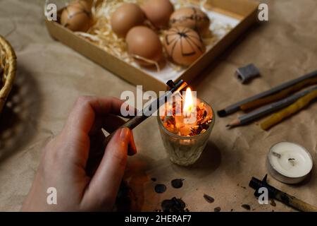 Female hand holding pen, pysachok, near flame and heating it. Preparing for painting Ukrainian Easter eggs decorated with folk designs using a wax res Stock Photo