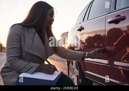 insurance agent examines the car. Accident claim process. African-American woman checking the damage to the car after an accident. Transportation conc Stock Photo
