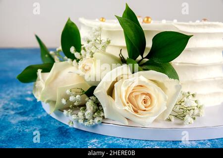 Wedding cake with white roses on blue background. Close up. Stock Photo