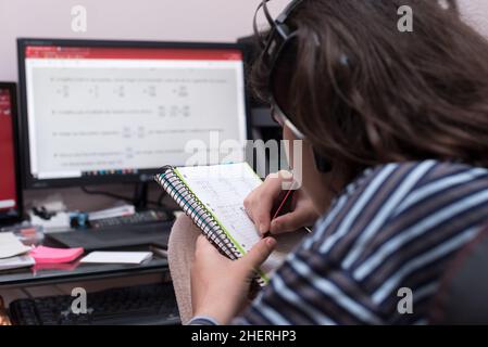 Transgender teenager seen from behind with headphones and microphone studying in front of computer, entertains himself by drawing and does not solve m Stock Photo