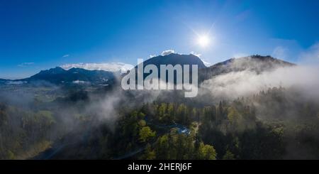 sunrise sunbeams over foggy mountains with clouds between forest trees in austria Stock Photo