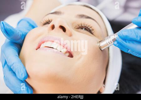 Closeup photo of smiling woman receiving face cleaning procedure in cosmetology clinic, vacuum cleaning. Stock Photo