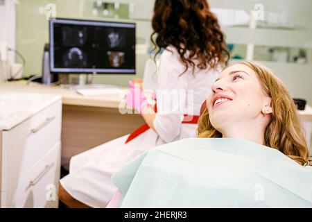 Beautiful young woman patient smiling for the doctor dentist while she looking at the teeth snapshot on the computer. Stock Photo