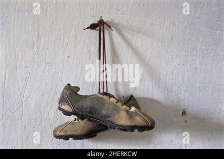 Hanging old leather football boots on nail in front of white wall Stock Photo