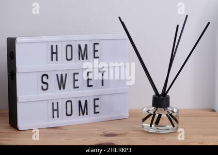 Lightbox with text HOME SWEET HOME and aroma reed diffuser on wooden table - Image Stock Photo