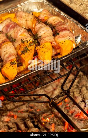 Tasty pumpkin slices wrapped in bacon baked on a grill. Autumn recipes. Delicious november dish. Shallow depth of field Stock Photo