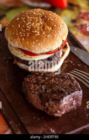 Delicious cheeseburger and beef steak on a cutting board. Tasty burger with cheese and tomato and a piece of beef meat Stock Photo