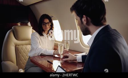 Businesswoman taking glass of champagne near blurred boyfriend in private plane Stock Photo