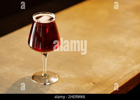 Glass with tasty red amber ale craft beer on table. Teku stemmed beer glass. Stock Photo