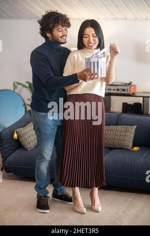 Man giving gift to smiling woman standing indoors Stock Photo