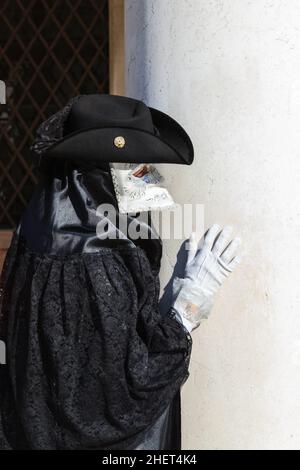 Man in historic bauta costume with tricorn black hat, tabarro mantle and white larva mask, Venice Carnival, Carnivale di Venezia, Veneto, Italy Stock Photo