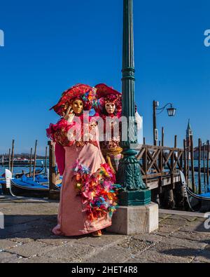 Man and woman in colourful historic Venetian fancy dress costumes, pose by the lagoon at Venice Carnival, Carnevale di Venezia, Italy Stock Photo
