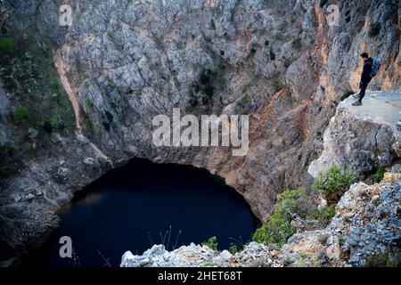 Hiker looking down into the Red lake in April at Imotski, Dalmatia, Croatia Stock Photo