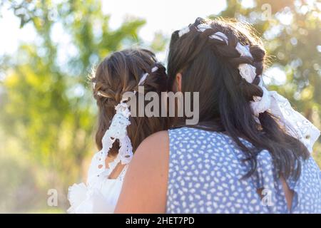 Rear view of mother and daughter sitting in nature wearing beautiful braids. Soft focus Stock Photo