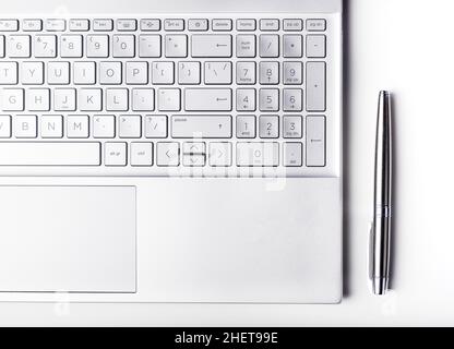 Laptop keyboard and pen of silver color, top view. Business and technology concept. Stock Photo