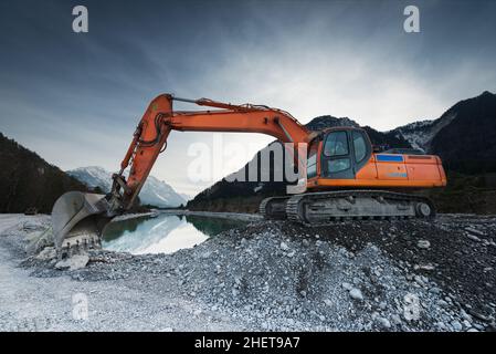 big shovel excavator standing on gravel stones before lake Stock Photo