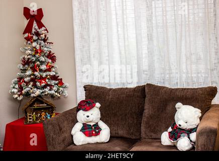 Two White Bears Sitting On Love Seat Next To Small Christmas Tree Stock Photo