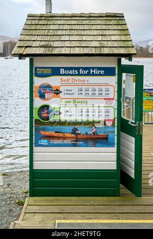 Wood built ticket hut at the end of a jetty on Lake Windermere, Cumbria, Uk showing self drive and row boat hire rates printed on a colourful sign Stock Photo