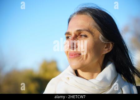 Profile side view portrait of attractive cheerful dreamy grey-haired middle-aged woman relaxing outdoors during sunny day Stock Photo