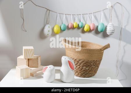 Fragment of the interior. Decorated children's room for Easter. A garland of plastic eggs on the wall. Ceramic rabbits and wooden cubes on the table. Stock Photo