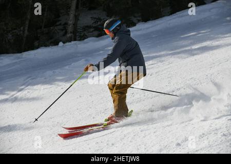 Skier rides down the slope on fresh powder snow in Stowe mountains, Vermont, USA. Winter sport. Motion photo.