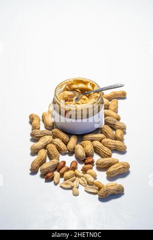 peanut butter in an open glass on a white background, next to scattered peanuts Stock Photo