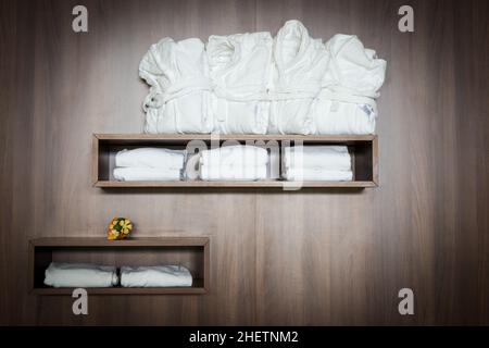 white bathrobes and towels stapled on brown wooden shelf with flowers Stock Photo