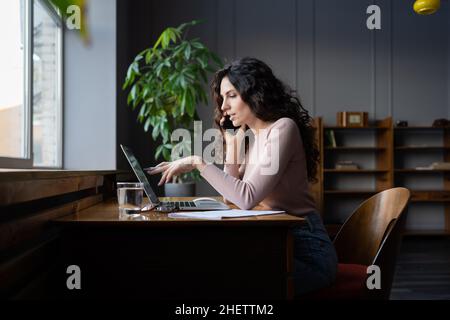 Young female entrepreneur talking on mobile phone and pointing at laptop screen, working in office Stock Photo