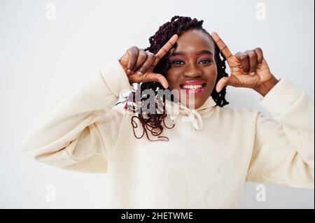African woman in hoodie stand against white wall and show frame on head by fingers. Stock Photo